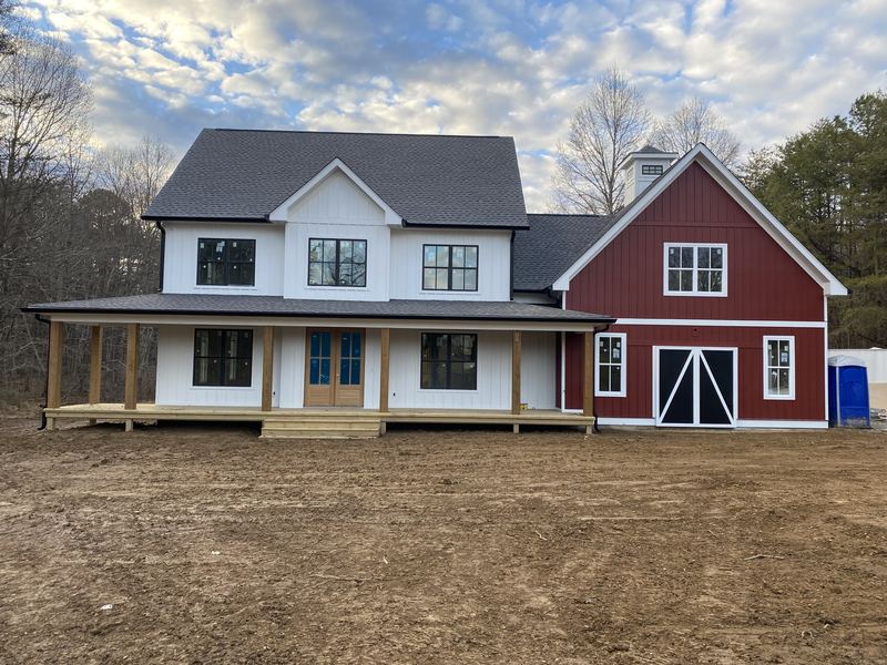 New construction modern farmhouse with attached red barn and wraparound porch