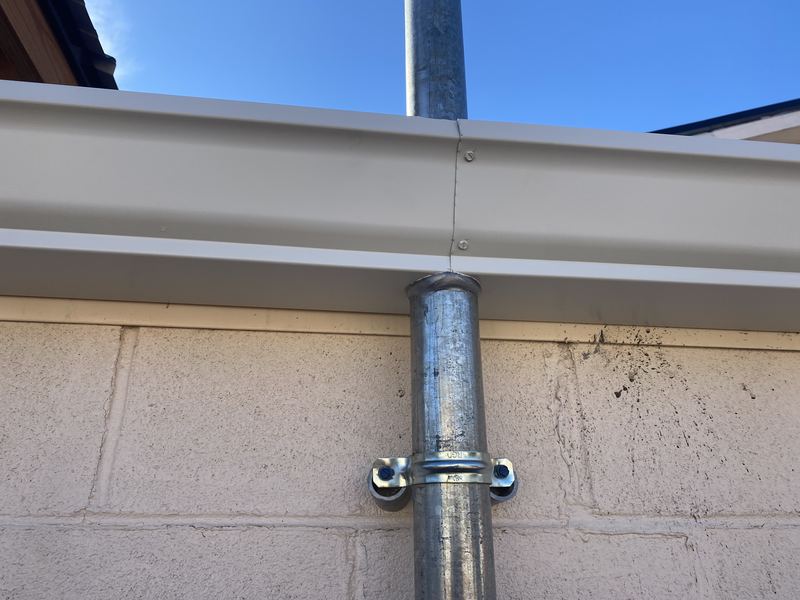 Round galvanized downspout installed through seamless K-style gutter